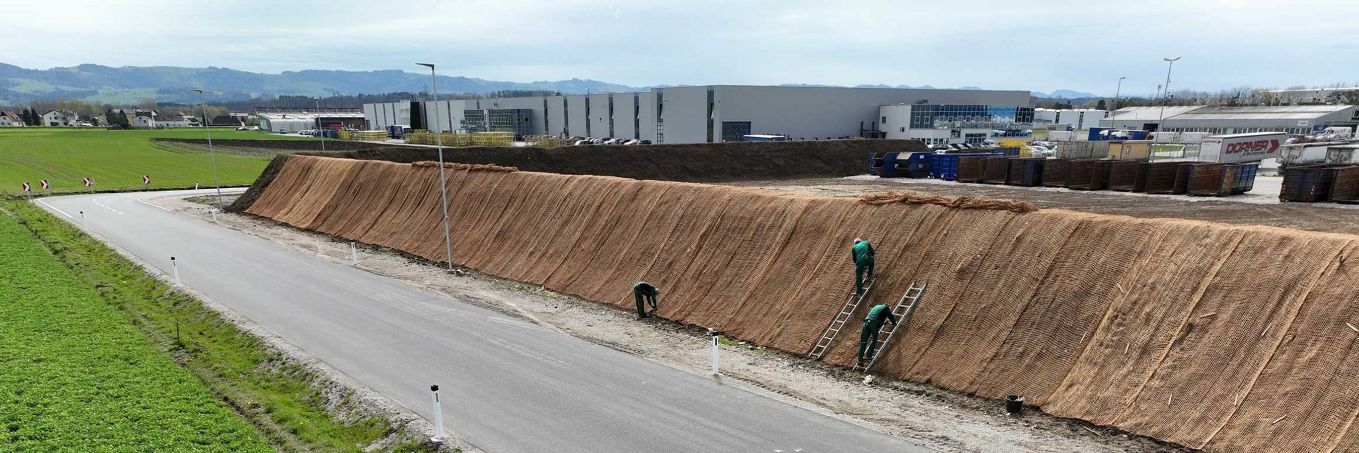 © Felbermayr/Nusime Biologisch abbaubares Kokosgeflecht und Arbeiter auf Leitern, die das Geflecht anbringen.