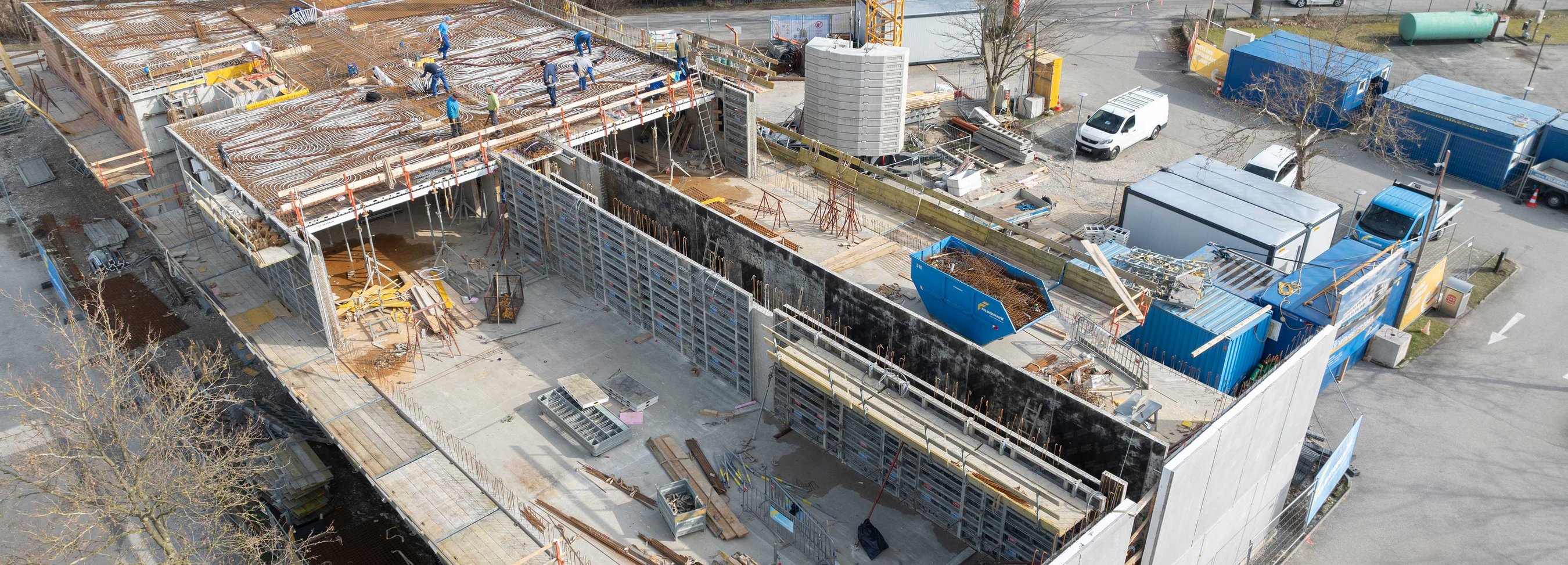 © Felbermayr/Weickinger Luftaufnahme einer Großbaustelle mit offenen Betonstrukturen, Baumaterialien, Containern und arbeitenden Personen auf der oberen Ebene.